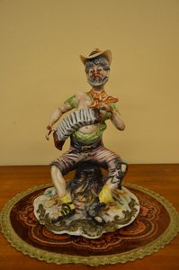 Porcelánová soška hudebníka s harmonikou