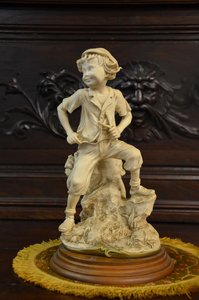 Porcelánová soška chlapce na skalce