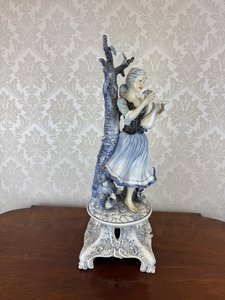 Porcelánová soška dívky u stromu s květinou a modrobílým podstavcem
